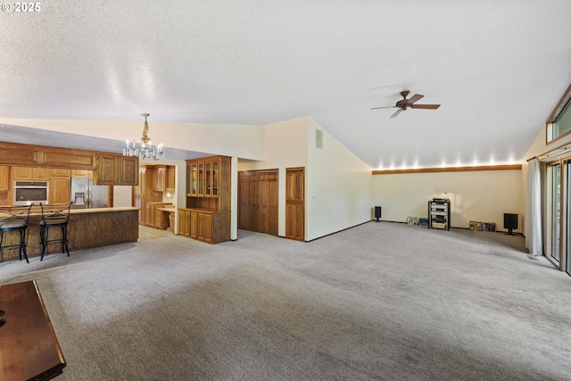 unfurnished living room with lofted ceiling, visible vents, light colored carpet, a textured ceiling, and ceiling fan with notable chandelier