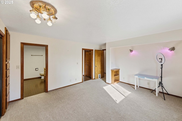 unfurnished bedroom featuring baseboards, an inviting chandelier, ensuite bathroom, and light colored carpet