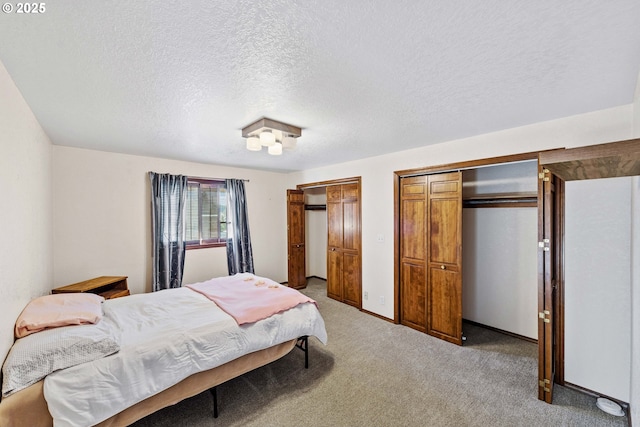 bedroom featuring light carpet, a textured ceiling, baseboards, and multiple closets