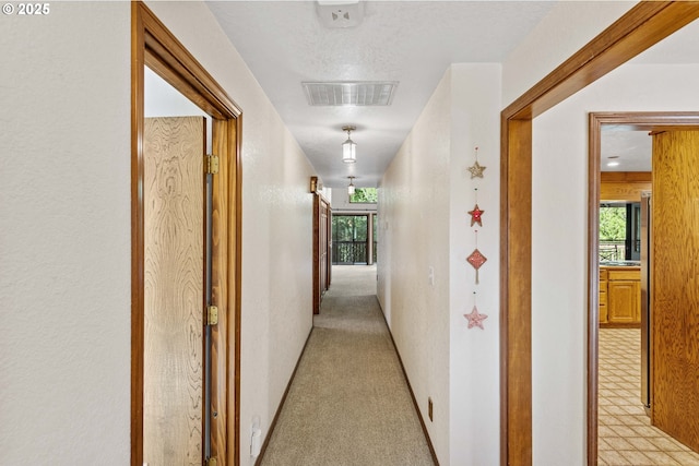 hall with light colored carpet, a healthy amount of sunlight, visible vents, and baseboards