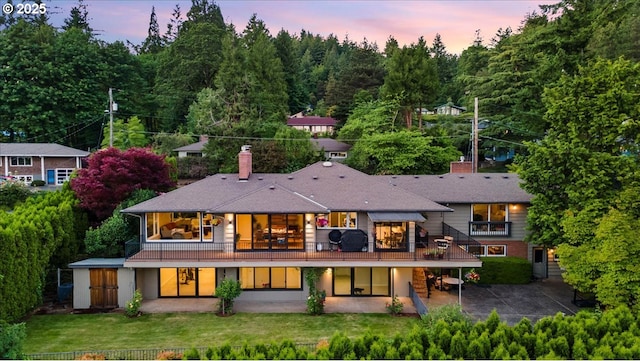 3132 SW Altadena Ter, Portland, OR 97239 - back of property at dusk with a patio, a chimney, a lawn, and concrete driveway