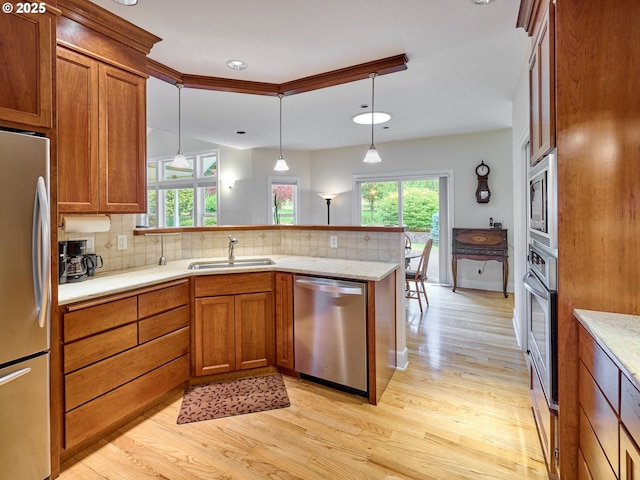 kitchen with appliances with stainless steel finishes, backsplash, sink, decorative light fixtures, and light hardwood / wood-style floors