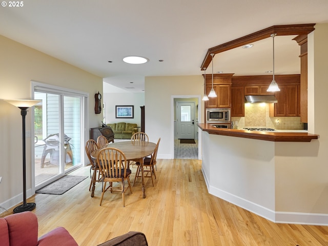 kitchen featuring stainless steel microwave, tasteful backsplash, kitchen peninsula, light hardwood / wood-style floors, and decorative light fixtures