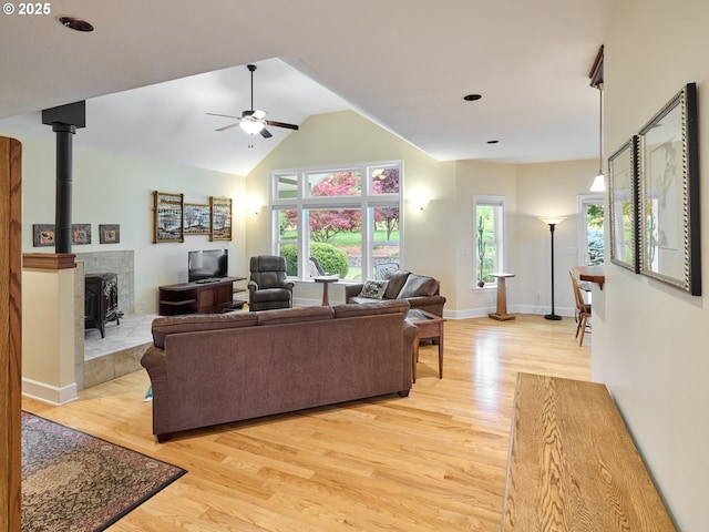 living room featuring ceiling fan, a healthy amount of sunlight, a wood stove, and light hardwood / wood-style flooring