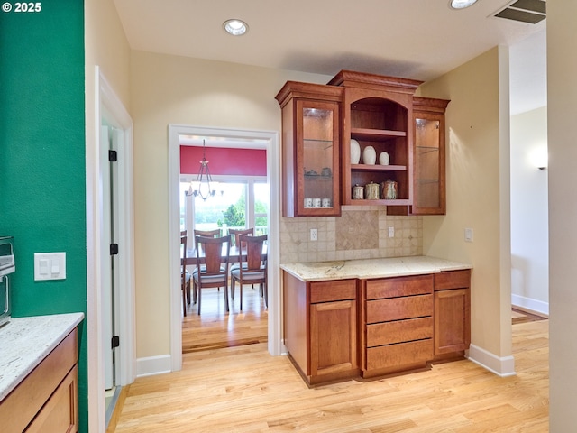 kitchen featuring light stone countertops, light wood-type flooring, backsplash, and a chandelier