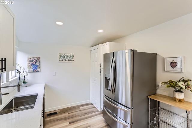 kitchen featuring white cabinets, stainless steel fridge with ice dispenser, light stone counters, and light hardwood / wood-style floors