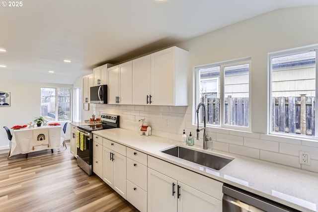 kitchen with white cabinetry, stainless steel appliances, decorative backsplash, light stone counters, and sink