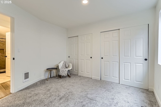 unfurnished bedroom featuring carpet, multiple closets, and heating unit