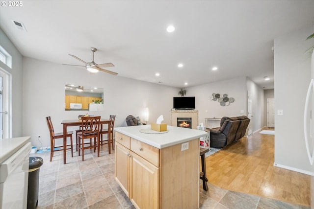 kitchen with recessed lighting, visible vents, light brown cabinetry, a glass covered fireplace, and white appliances