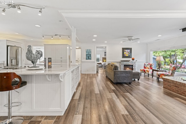 9202 Phey Ln, Florence, OR 97439 - kitchen with a glass covered fireplace, wood finished floors, a kitchen bar, white cabinetry, and stainless steel fridge with ice dispenser