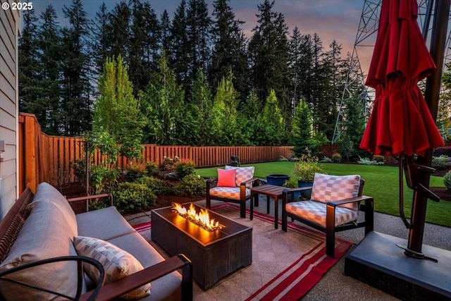 patio terrace at dusk featuring a yard, a fenced backyard, and an outdoor fire pit