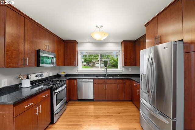 kitchen with appliances with stainless steel finishes, a sink, light wood-type flooring, brown cabinets, and recessed lighting