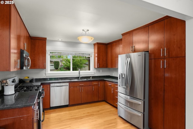 kitchen featuring stainless steel appliances, a sink, light wood finished floors, brown cabinets, and pendant lighting