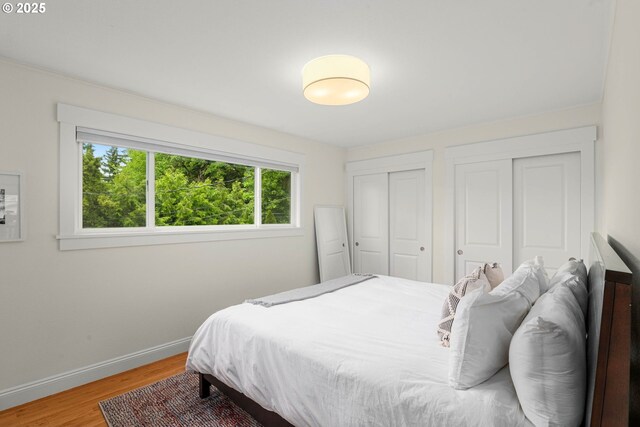 bedroom featuring two closets, wood finished floors, and baseboards