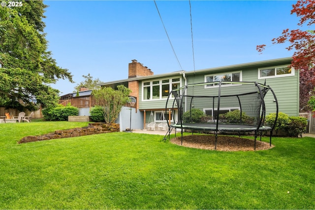 rear view of property featuring a trampoline, a chimney, and a lawn