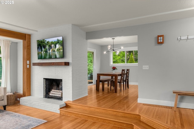 living room with wood finished floors, baseboards, a chandelier, and a brick fireplace