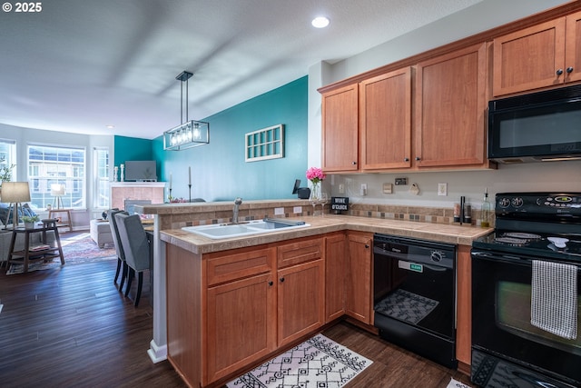 kitchen featuring dark wood finished floors, open floor plan, a peninsula, black appliances, and a sink