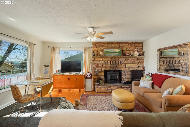 living room with a textured ceiling, a stone fireplace, light wood-type flooring, and a ceiling fan