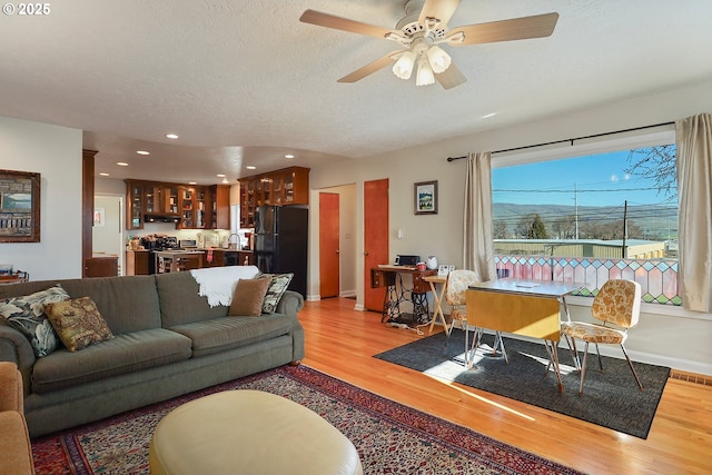 living area featuring a ceiling fan, visible vents, a textured ceiling, and light wood finished floors