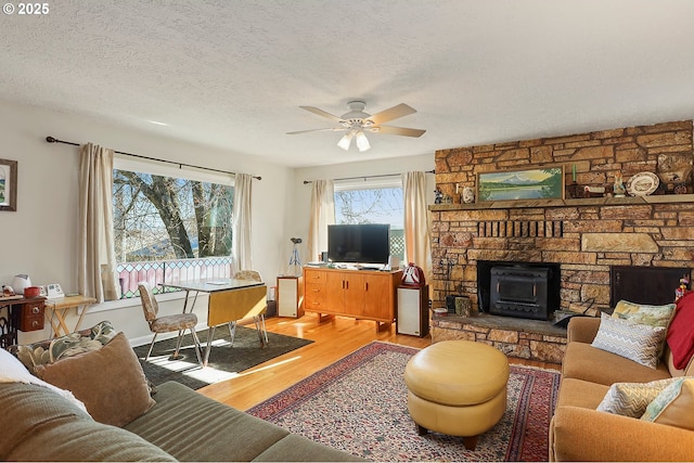 living area featuring light wood-style flooring, a fireplace, ceiling fan, and a textured ceiling