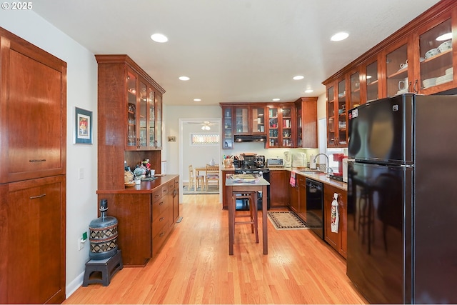 kitchen with light wood-style flooring, under cabinet range hood, a sink, black appliances, and glass insert cabinets