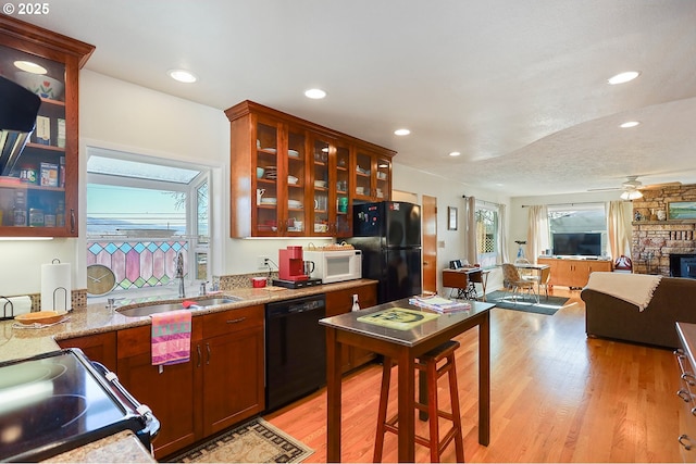 kitchen with light wood-type flooring, a fireplace, a sink, and black appliances