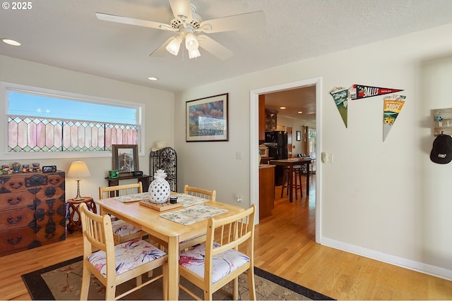 dining room with a textured ceiling, light wood-type flooring, a ceiling fan, and baseboards