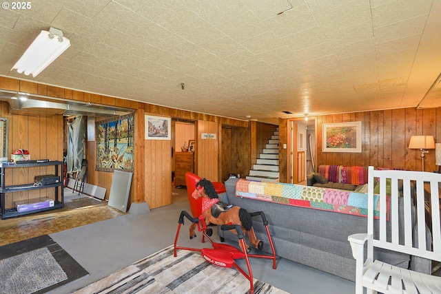 living area featuring concrete flooring, wooden walls, and stairs