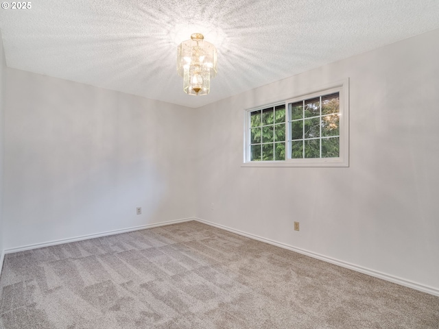 carpeted spare room featuring a textured ceiling, baseboards, and a chandelier