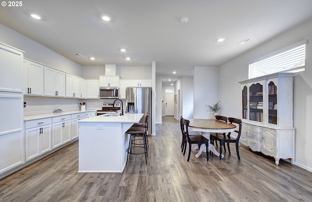kitchen with stainless steel appliances, a center island with sink, a sink, dark wood finished floors, and recessed lighting