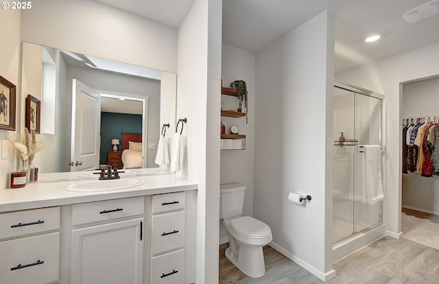 ensuite bathroom featuring a stall shower, vanity, toilet, and baseboards