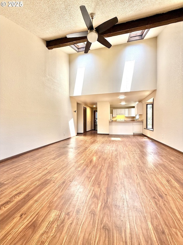 2011/2013 Ohio Ave, North Bend, OR 97459 - unfurnished living room featuring a skylight, high vaulted ceiling, ceiling fan, beam ceiling, and light wood-style floors