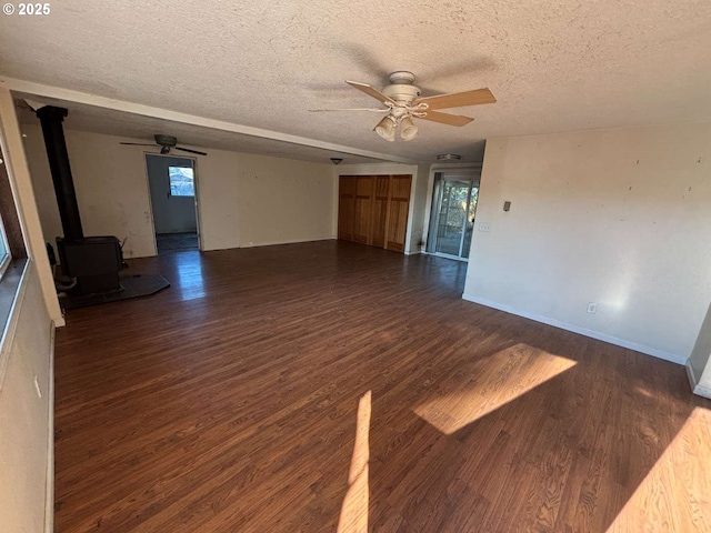 unfurnished living room with a textured ceiling, a wood stove, a ceiling fan, and wood finished floors