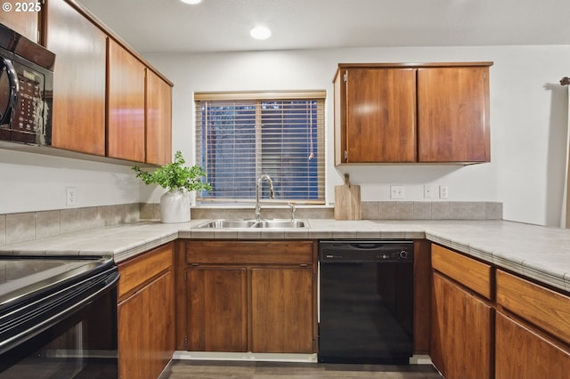 kitchen featuring brown cabinetry, a sink, tile countertops, and black appliances