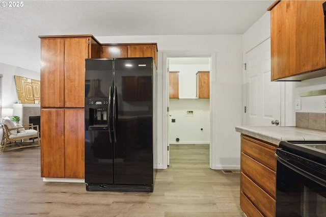 kitchen featuring light wood finished floors, baseboards, brown cabinets, tile countertops, and black appliances