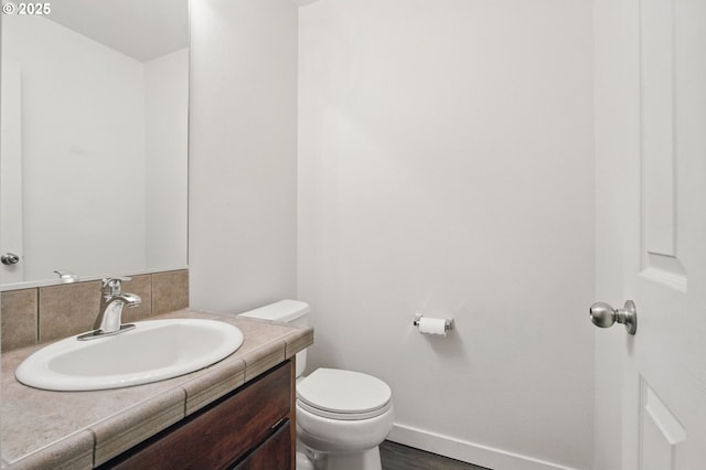 bathroom with baseboards, wood finished floors, vanity, and toilet