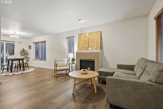 living area featuring wood finished floors, a tiled fireplace, baseboards, and an inviting chandelier