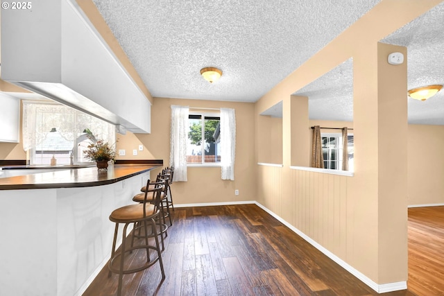 523 65th St, Springfield, OR 97478 - kitchen with a textured ceiling, hardwood / wood-style flooring, baseboards, a breakfast bar area, and dark countertops