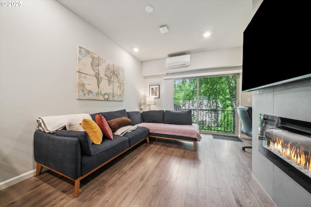 living room with a wall mounted AC, a glass covered fireplace, wood finished floors, and recessed lighting