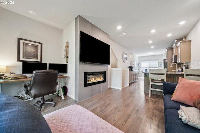 living room featuring wood finished floors, an office area, recessed lighting, a tiled fireplace, and baseboards