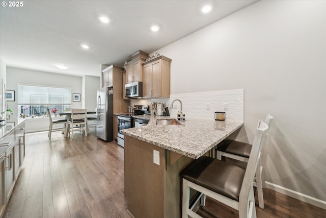 kitchen featuring appliances with stainless steel finishes, a sink, a breakfast bar area, light stone counters, and tasteful backsplash