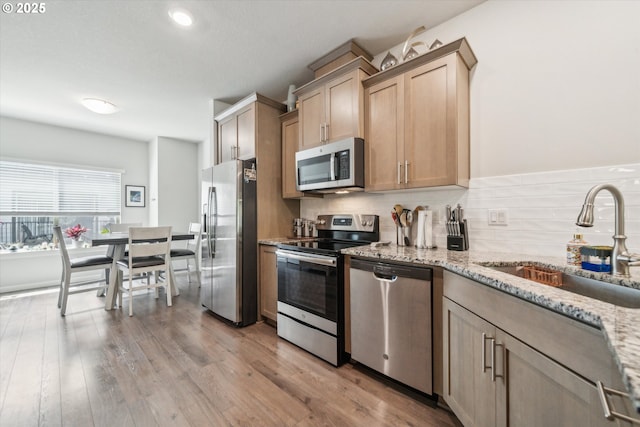 kitchen featuring appliances with stainless steel finishes, a sink, backsplash, light stone countertops, and recessed lighting