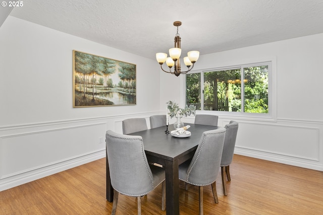 13555 SW Hiteon Ct, Beaverton, OR 97008 - dining area with a chandelier, wood finished floors, a decorative wall, a wainscoted wall, and a textured ceiling