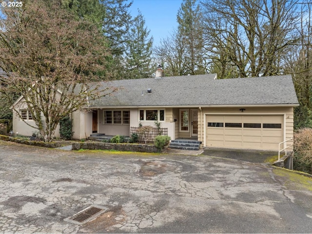 ranch-style home with an attached garage, a shingled roof, a chimney, and aphalt driveway