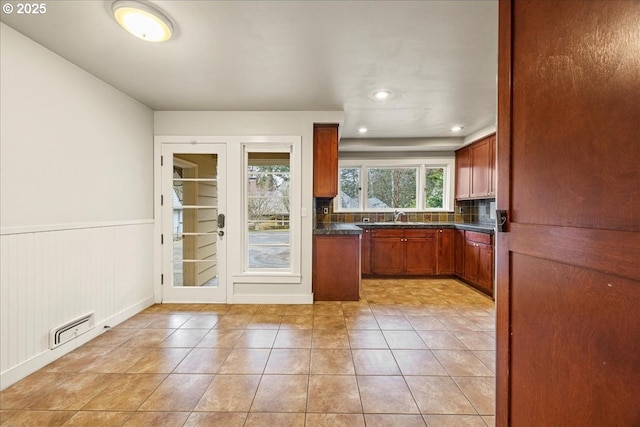 kitchen featuring light tile patterned floors, dark countertops, visible vents, brown cabinetry, and wainscoting