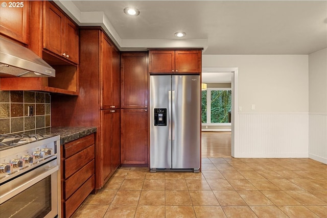 kitchen with a wainscoted wall, light tile patterned floors, stainless steel appliances, decorative backsplash, and under cabinet range hood