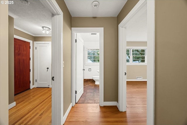 hallway with baseboards, light wood-style flooring, and a textured ceiling