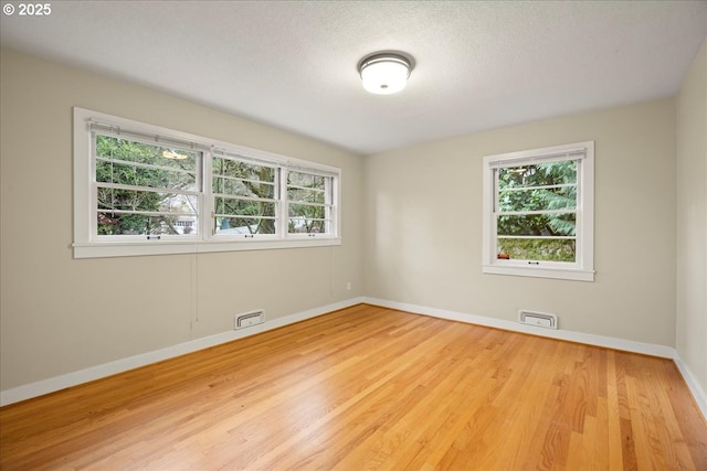 empty room with plenty of natural light, wood finished floors, and visible vents