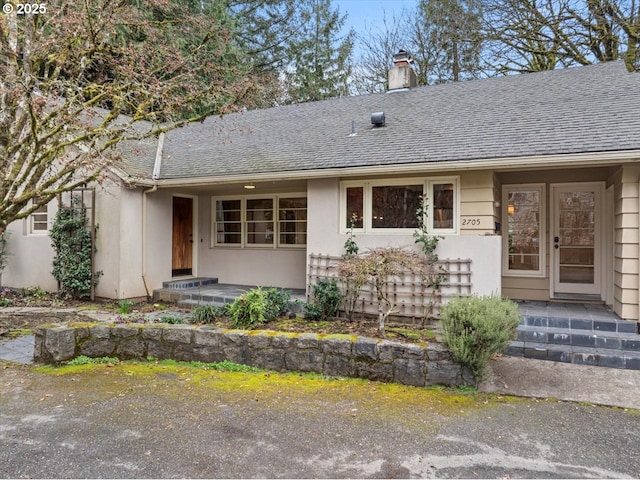 view of exterior entry featuring stucco siding, a chimney, and roof with shingles