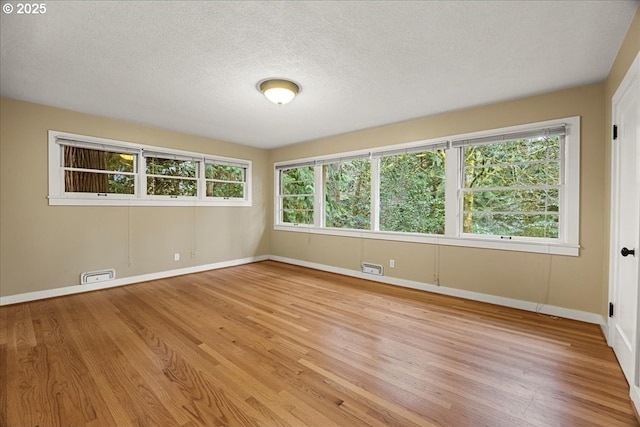 spare room with light wood-style flooring, visible vents, and a wealth of natural light